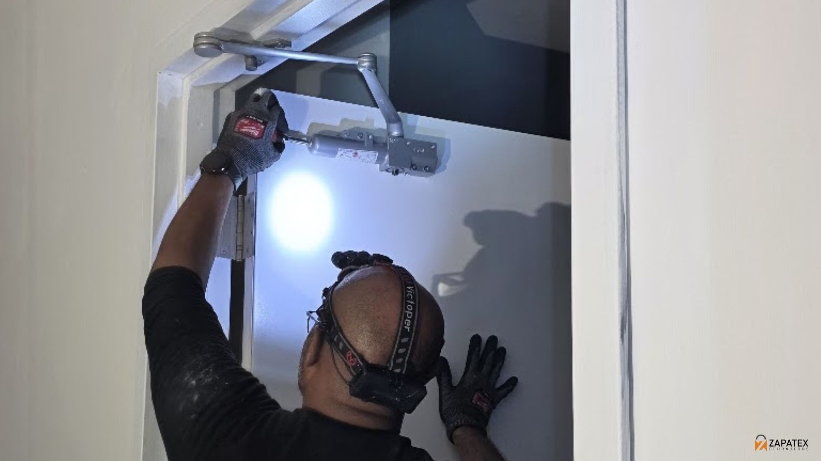 Tecnico de espaldas ajustando las valvulas de un mecanismo plateado en la parte superior de una puerta blanca
